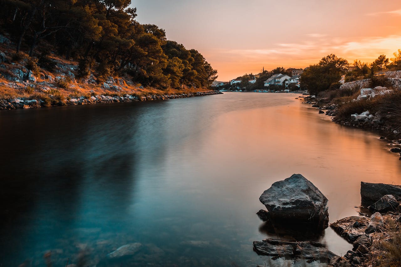 Peaceful river scene at sunset with trees and rocks creating an idyllic landscape.